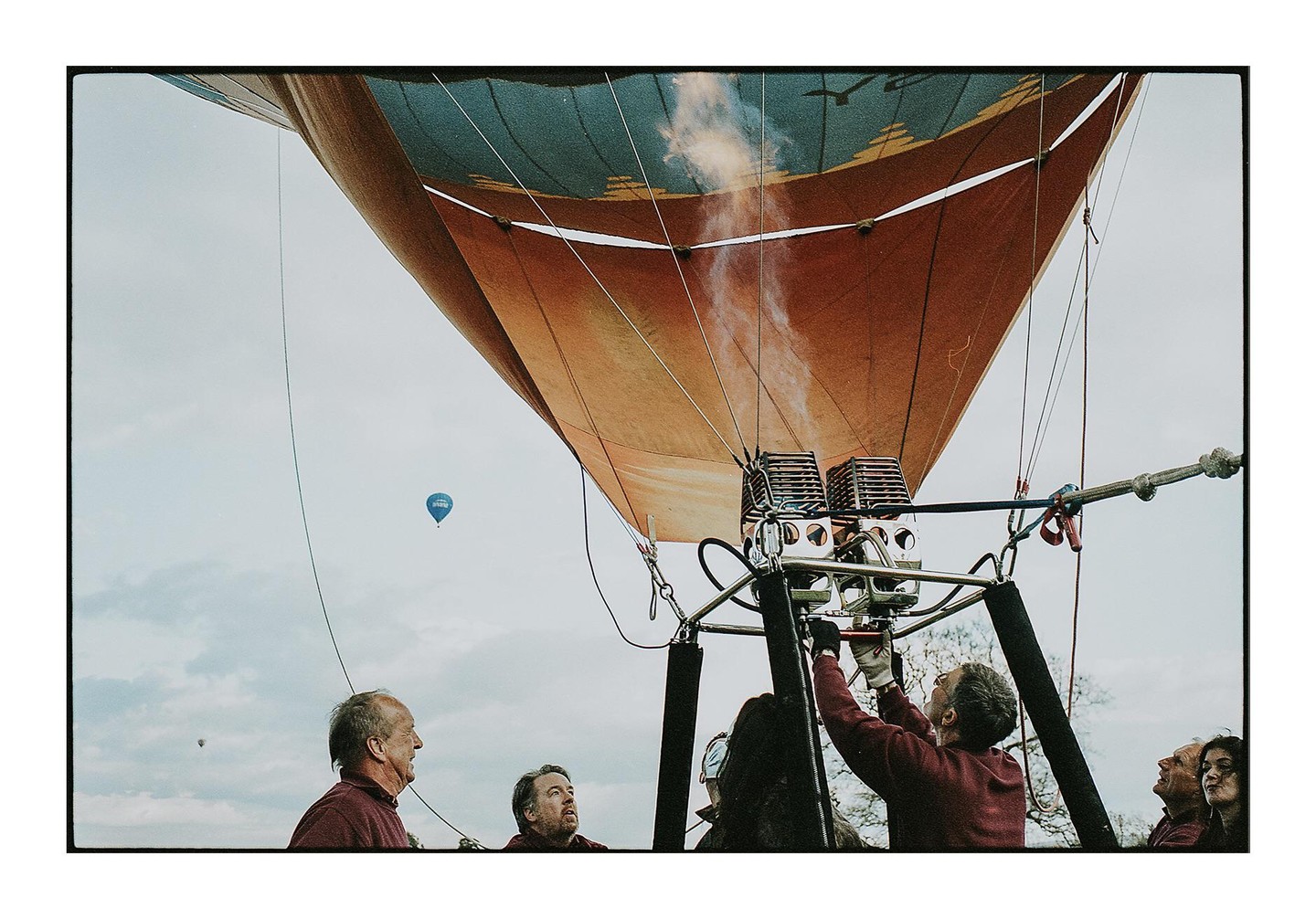 A group of people are preparing a hot air balloon for flight, with another balloon visible in the distance.
