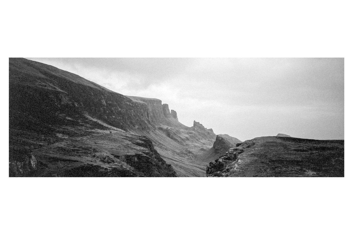 A panoramic view shows a rugged mountain landscape under a cloudy sky.