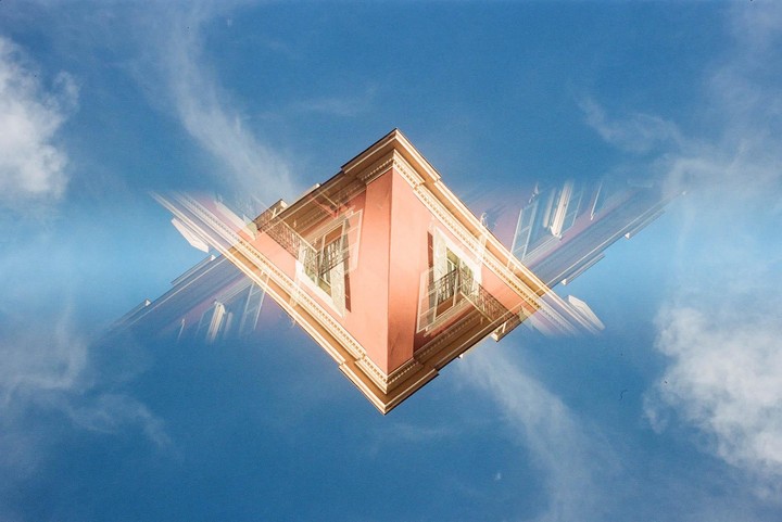 A building with a red facade and white shutters is shown in a multiple exposure against a blue sky with clouds.