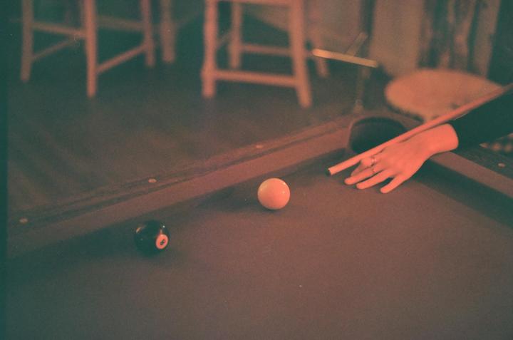 A person's hand holds a pool cue, aiming at a white cue ball on a pool table with an 8-ball nearby.