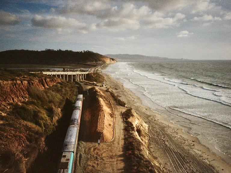 A train travels along a track next to a beach with waves crashing on the shore.