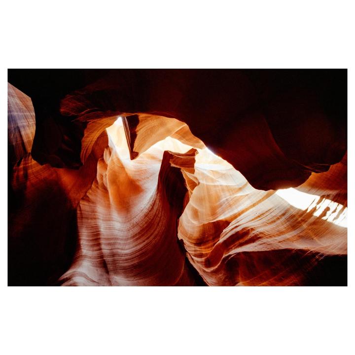 Light streams into a slot canyon, illuminating its wavy, colorful walls.