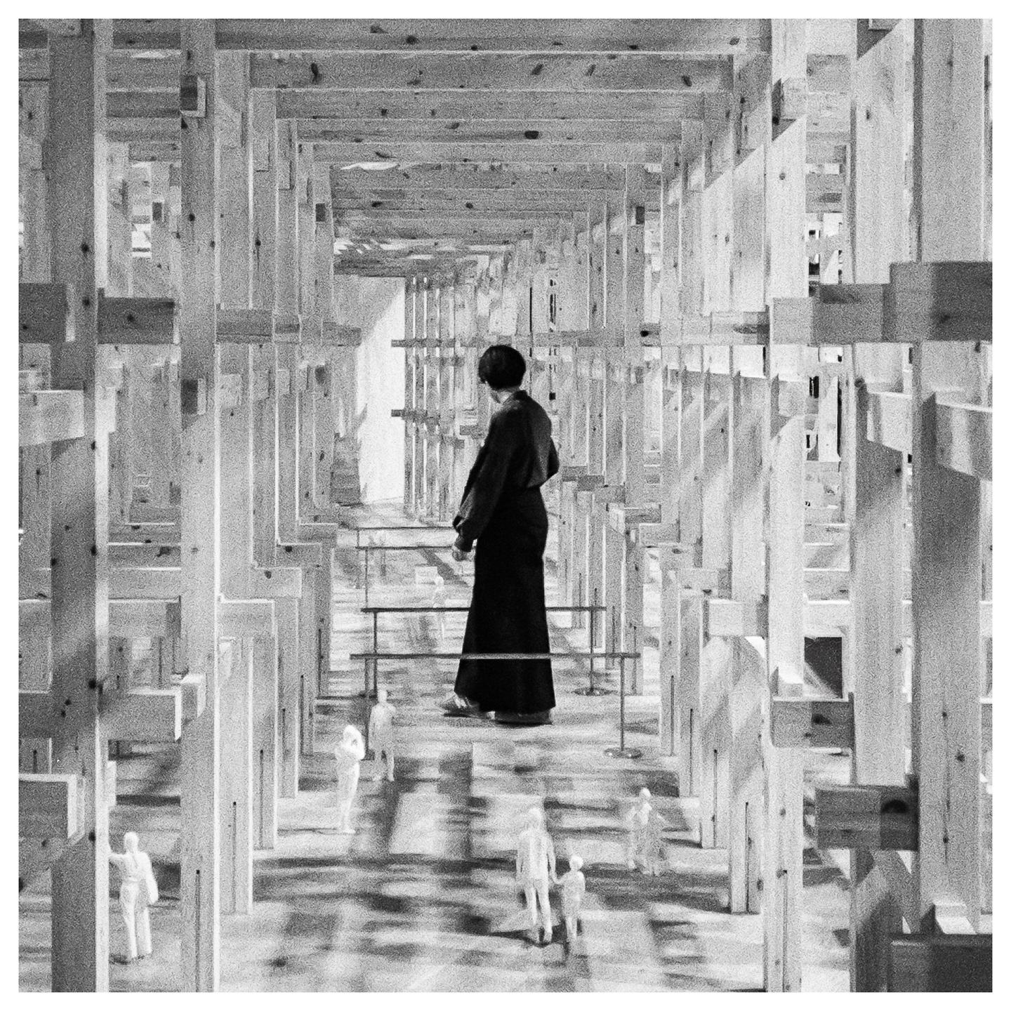 A woman stands in a room constructed from many wooden beams, looking down at small figures on the floor.