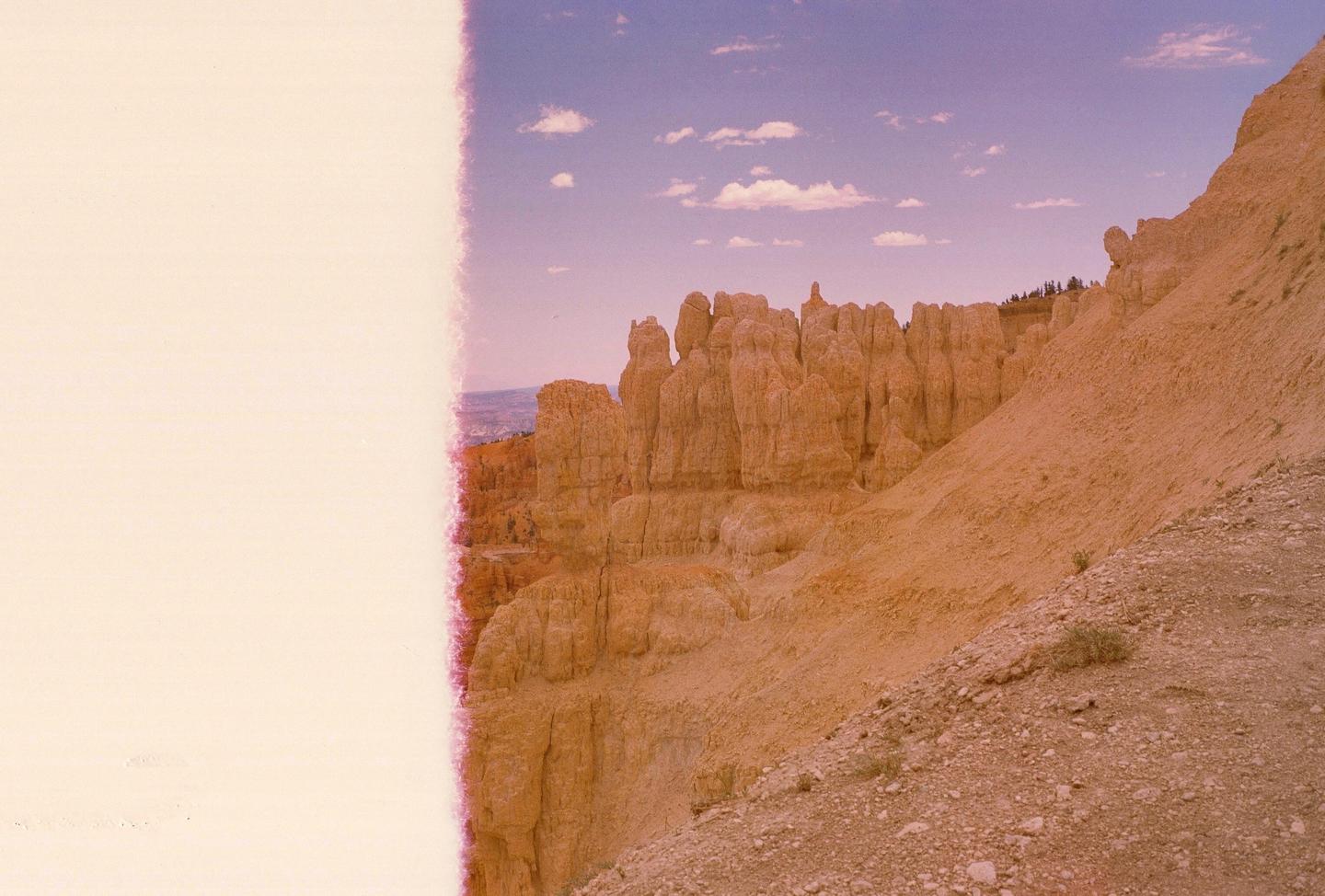 A desert landscape shows rock formations under a sky with clouds.