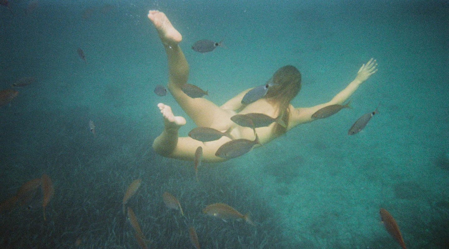 A woman swims underwater surrounded by fish.