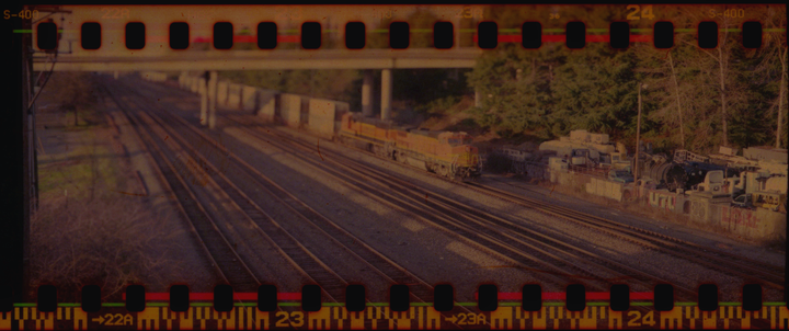 A train is visible on multiple tracks next to a wall covered in graffiti, with trees and an overpass in the background.