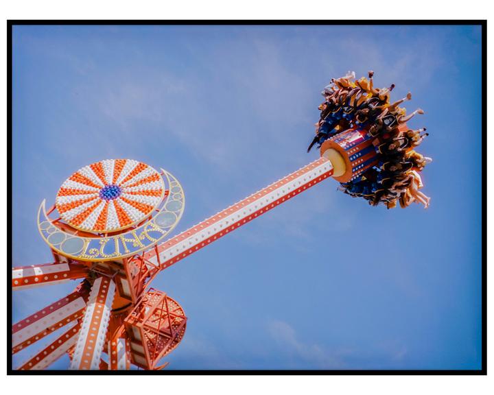 A group of people are riding a carnival ride against a clear blue sky.