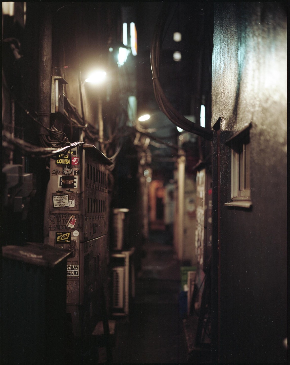 A narrow alleyway in Shinjuku, Tokyo, is illuminated by a single bright light.