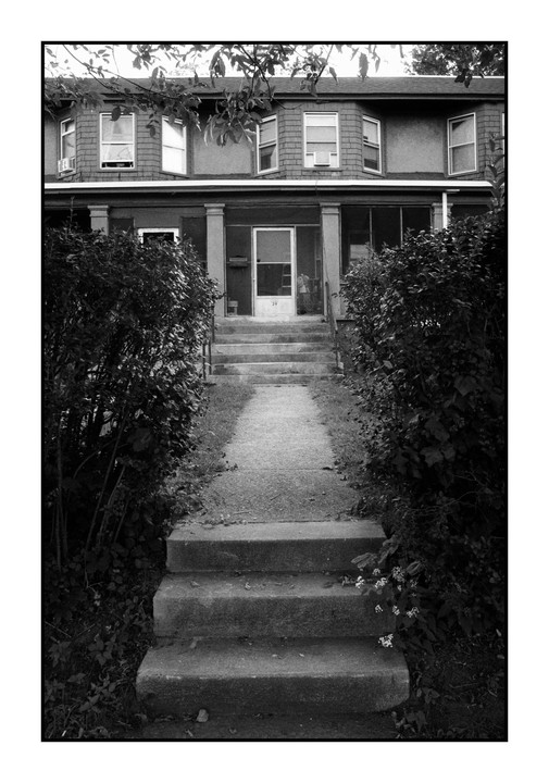 A path and steps lead up to a house with a porch and many windows.