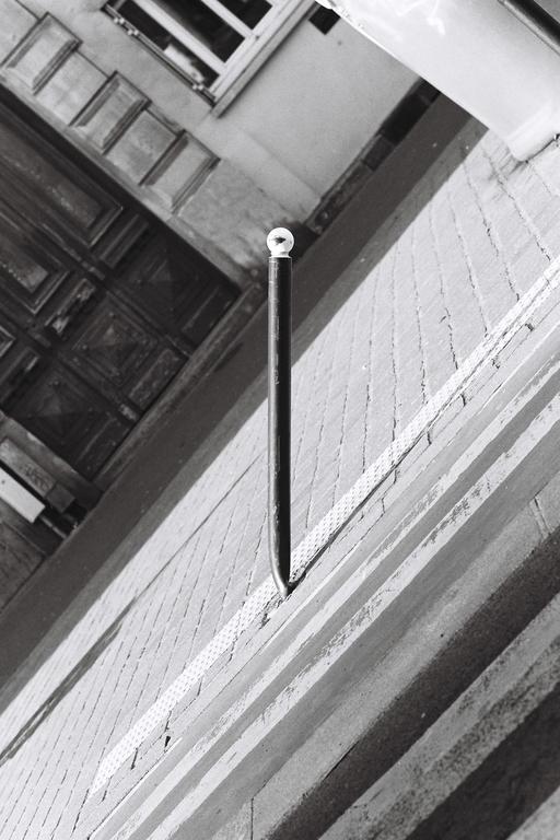 A black pole with a white spherical top is planted in a brick wall, casting a shadow.