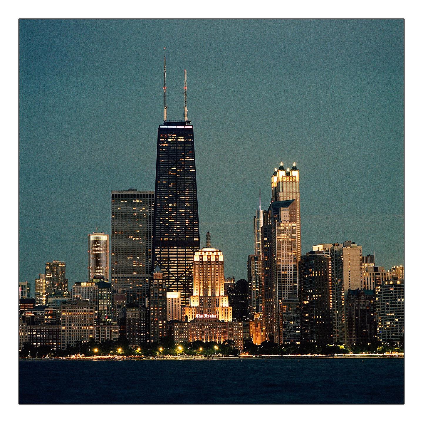 A city skyline with many illuminated buildings is visible from across a body of water at twilight.