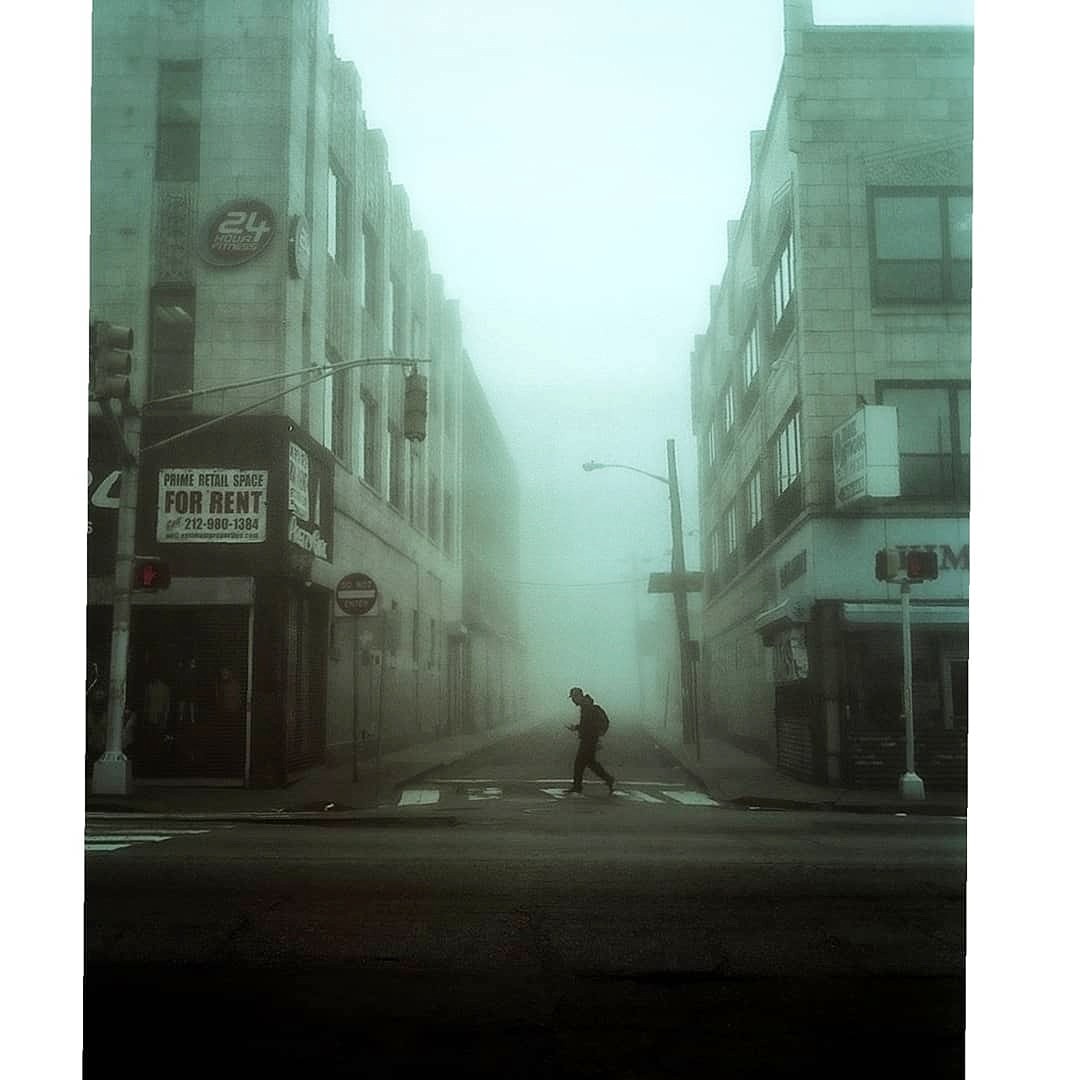 A man crosses a street between two buildings on a foggy day in Jersey City.