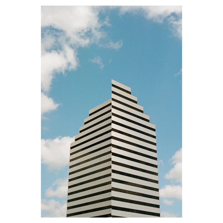 A tall, striped building with a stepped roofline stands against a blue sky with white clouds.