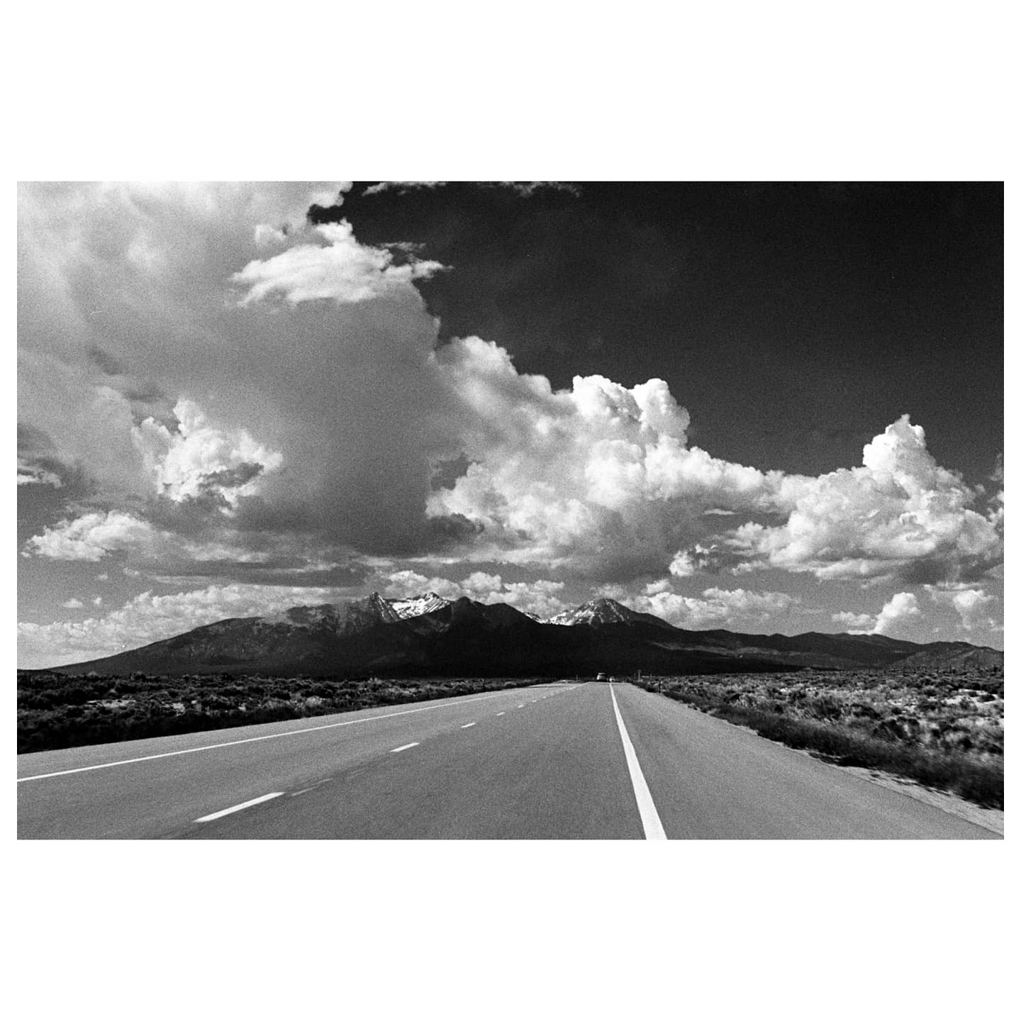 A long road leads towards snow-capped mountains under a dramatic cloudy sky.