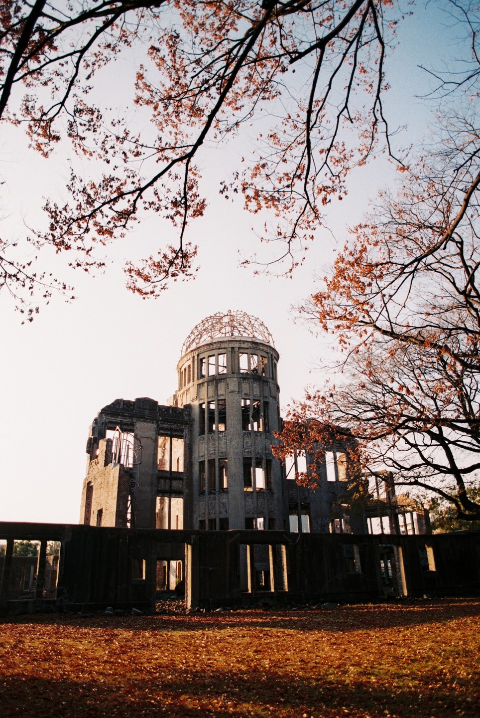 The Hiroshima Peace Memorial is visible through autumn tree branches and foliage.