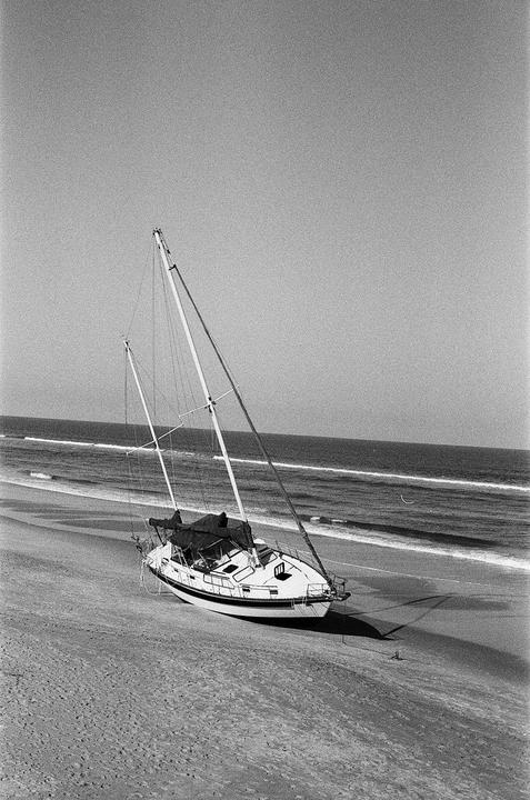 A sailboat is beached on the sand next to the ocean with waves breaking.