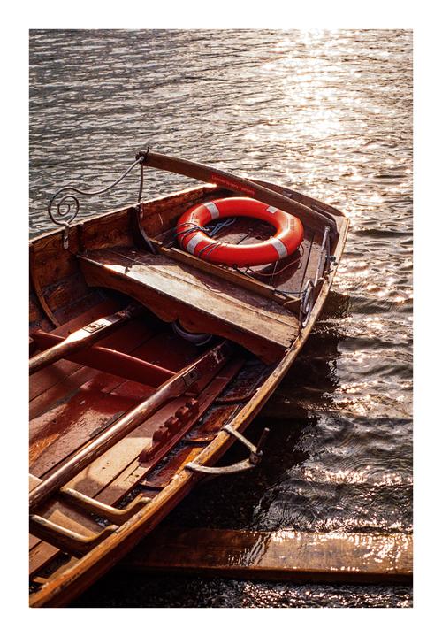 A wooden rowboat with a life preserver and oars sits in the water, reflecting the golden hour light.