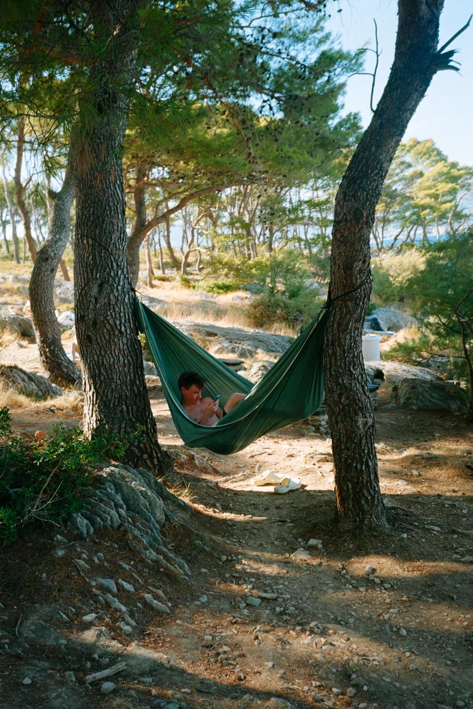 A man is relaxing in a green hammock tied between two trees in a forest.