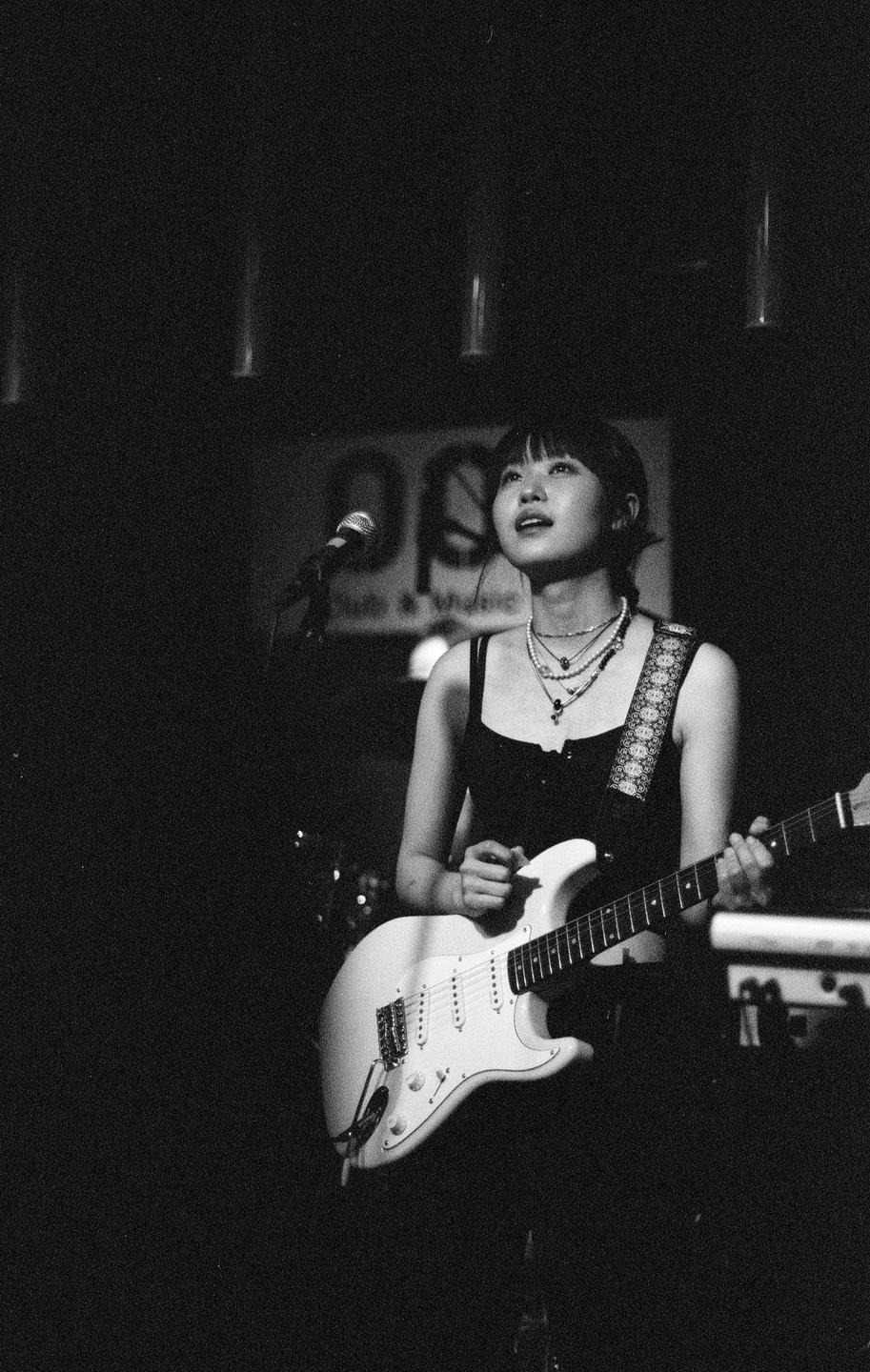 A woman plays an electric guitar on a stage with a microphone in the background.