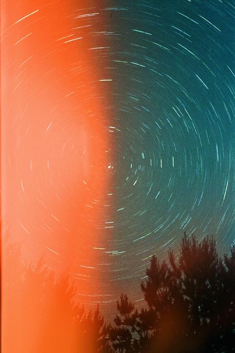 Star trails are visible in the night sky above trees, with a strong orange light source on the left.