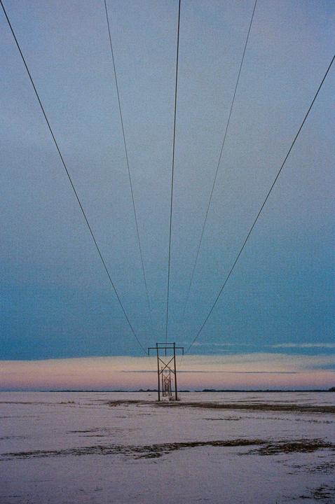 A power line stretches across a snowy field under a blue and pink sky.
