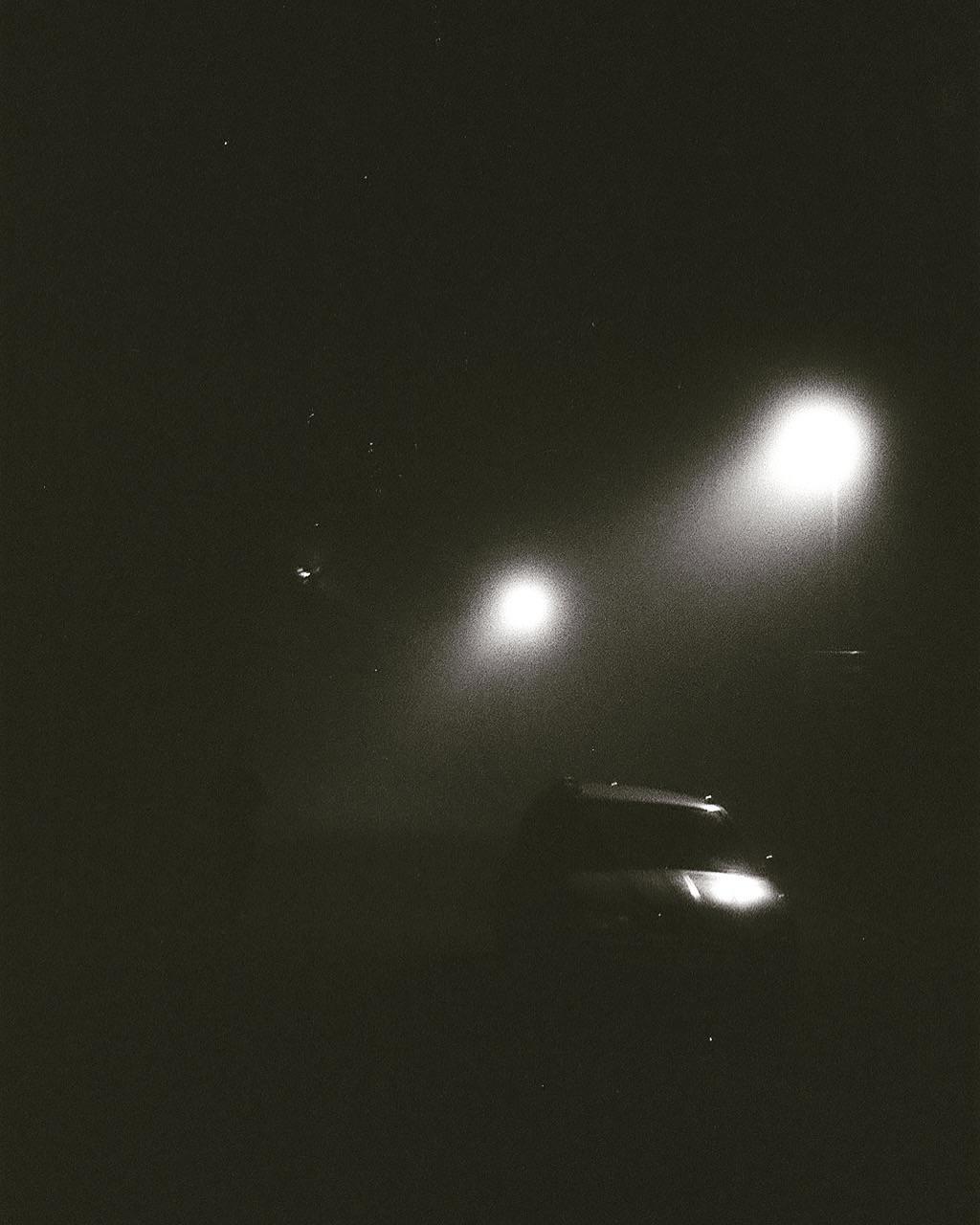 A car is visible in the dark with two bright lights in the background.