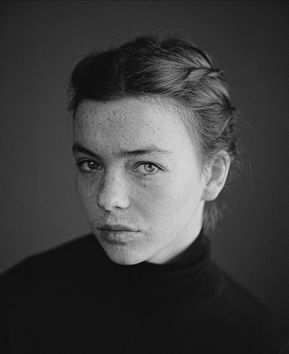 A woman with freckles and braided hair looks directly at the viewer.
