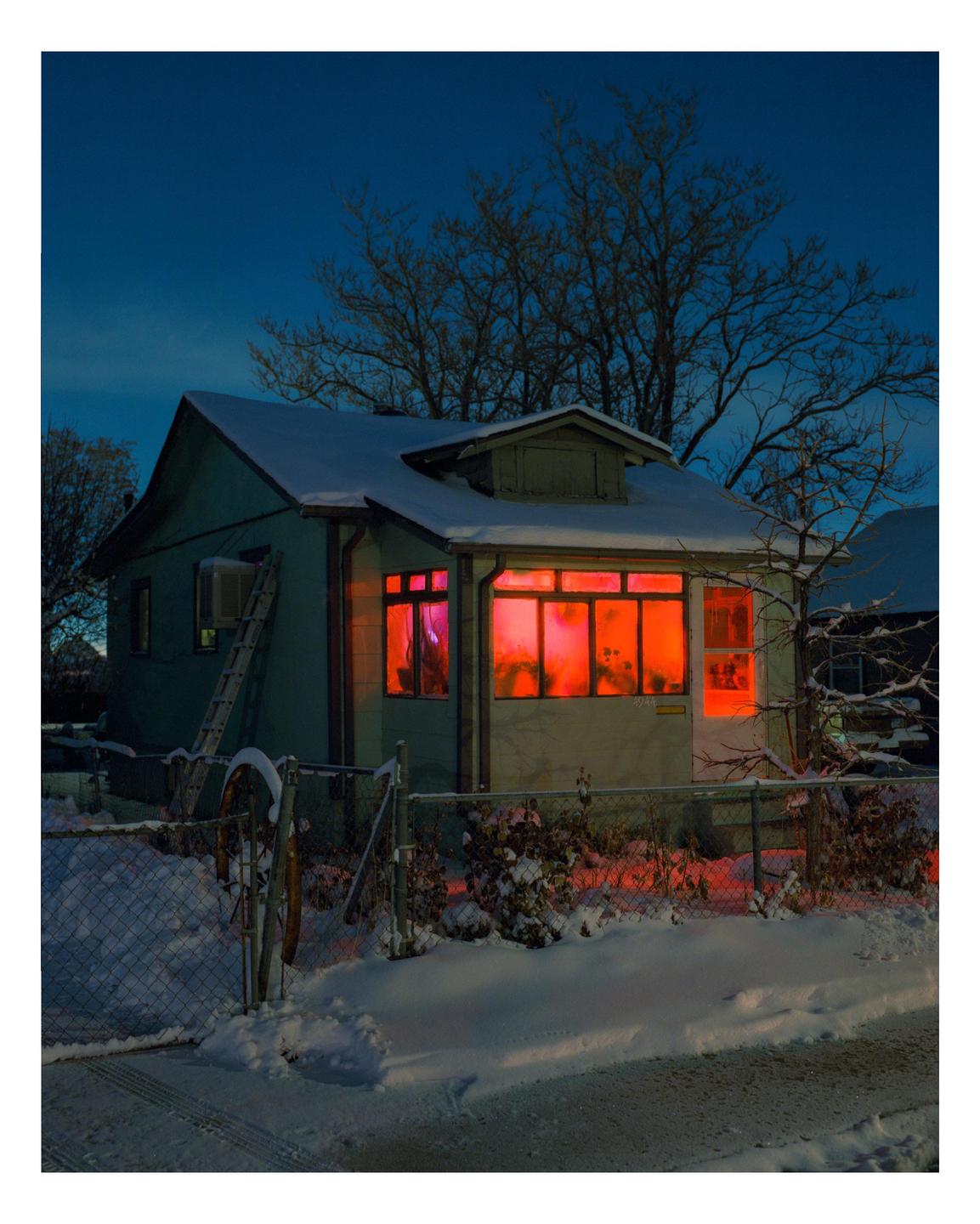 A house with glowing red windows stands in a snowy landscape at night.