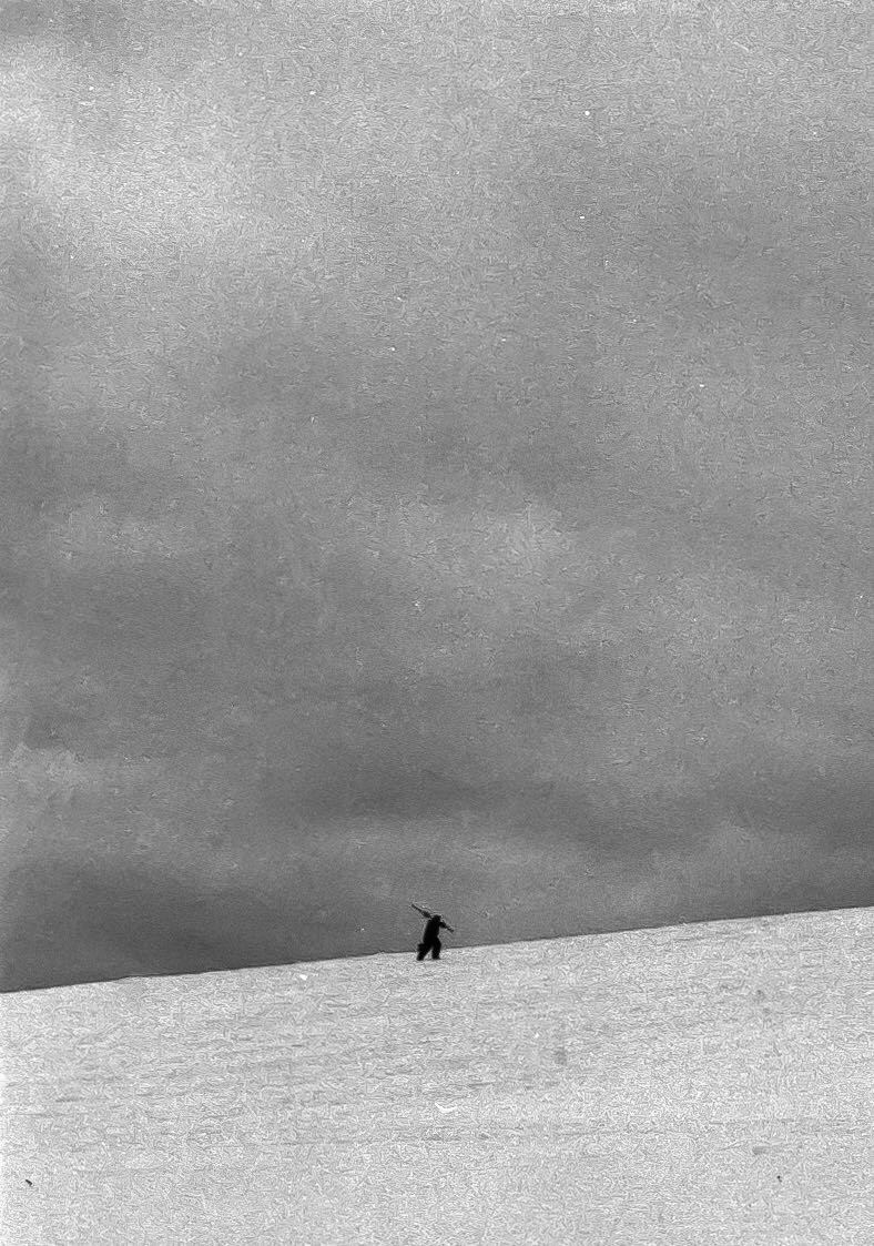 A person stands on a snow-covered hill under a cloudy sky.