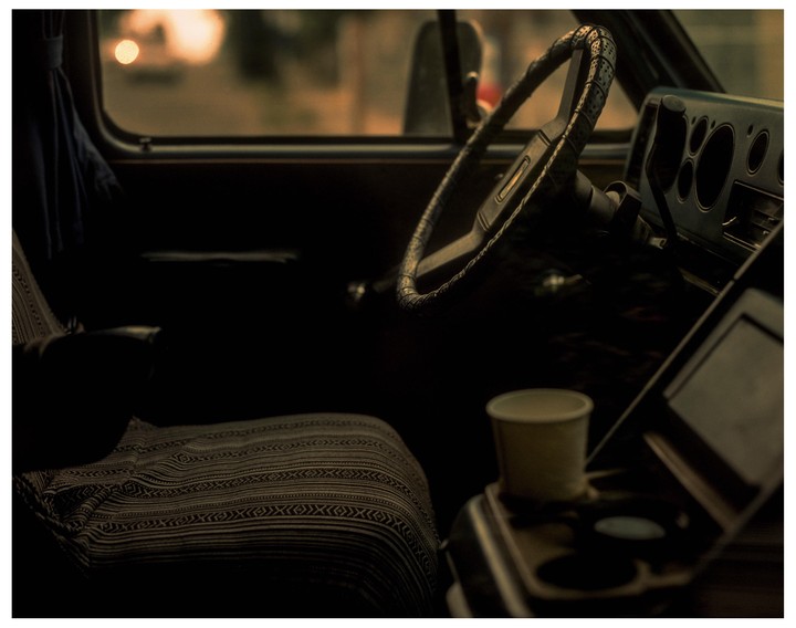 The interior of a van is visible, showing the steering wheel, dashboard, a patterned seat, and a paper cup in a cup holder.