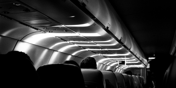 Light streams through the windows of an airplane cabin, illuminating the ceiling and the tops of passenger seats.