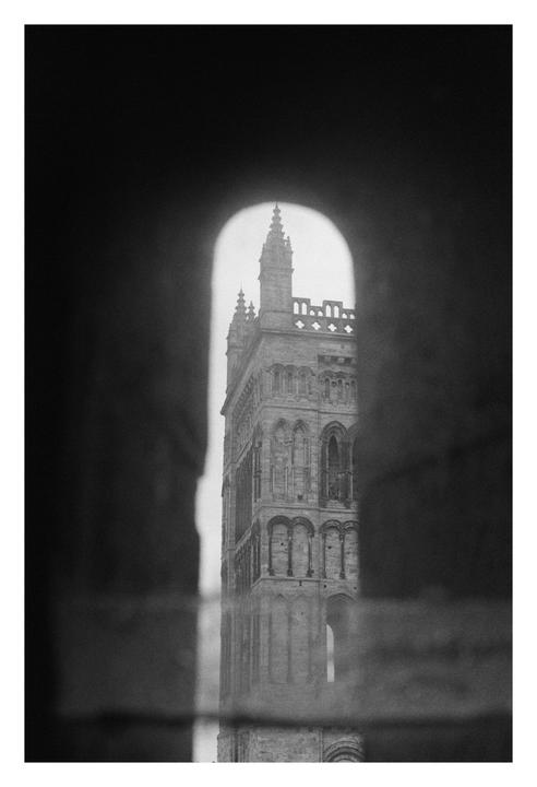 A tall, ornate building is visible through an arched opening in a black and white photograph.
