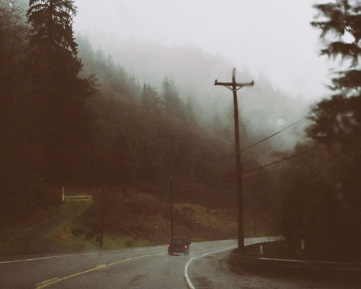 A car drives on a winding road through a foggy, forested landscape with a utility pole on the right.