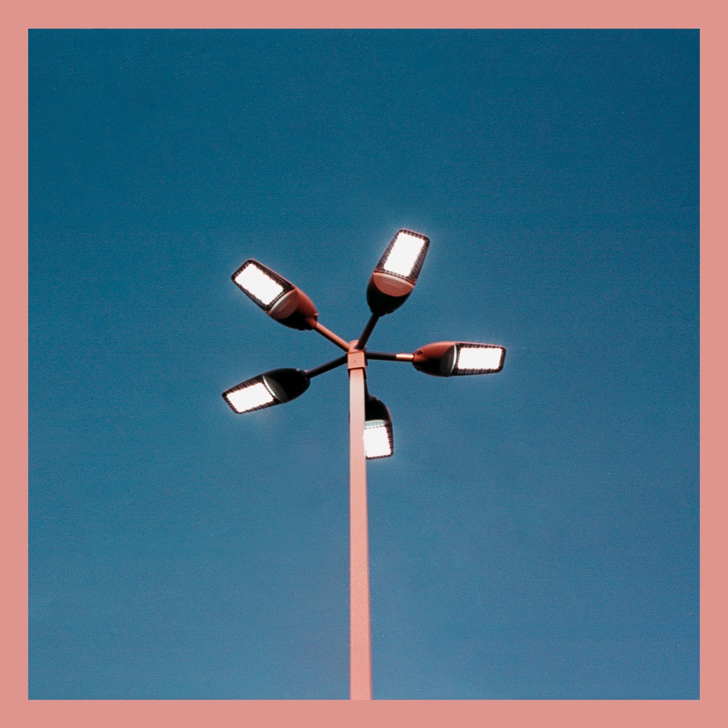 A street light with five lamps points in different directions against a clear blue sky.