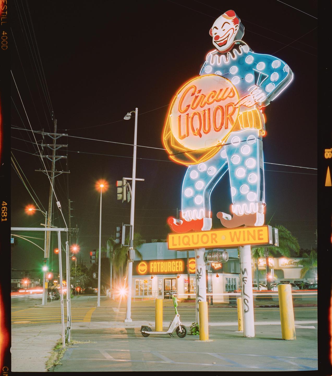 A large neon clown sign for Circus Liquor stands illuminated at night next to a street with light trails from cars.