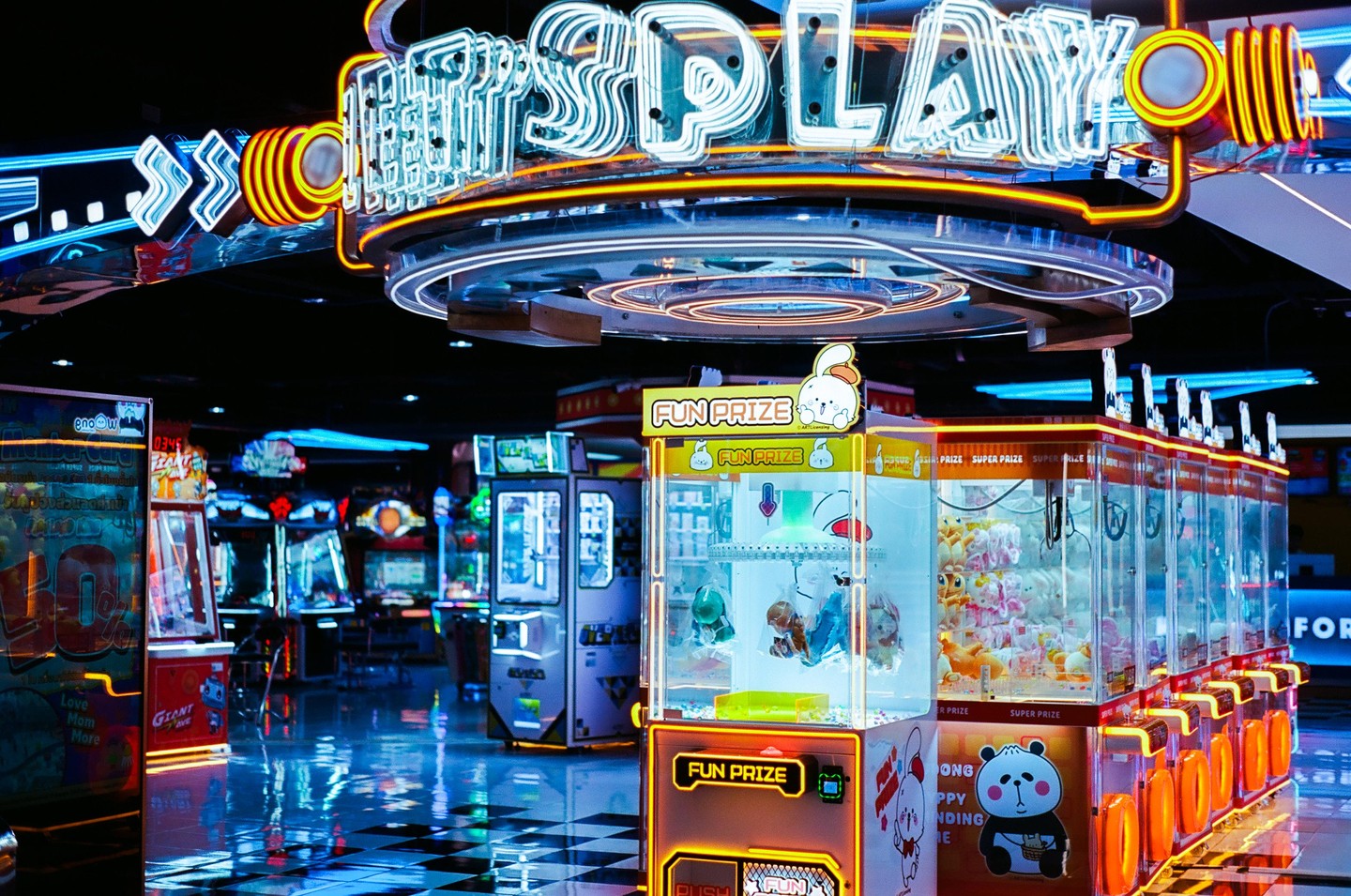 A neon sign for "SPLAY" hangs above an arcade with claw machines and other games.