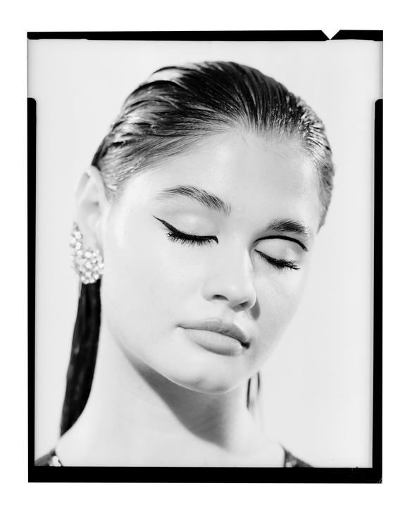A woman with closed eyes and slicked-back hair wears a large, ornate earring.