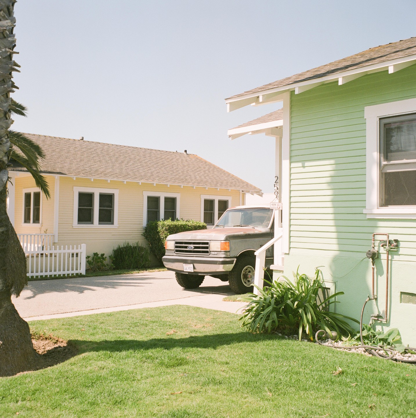 A pickup truck is parked in front of a light green house with a yellow house in the background.