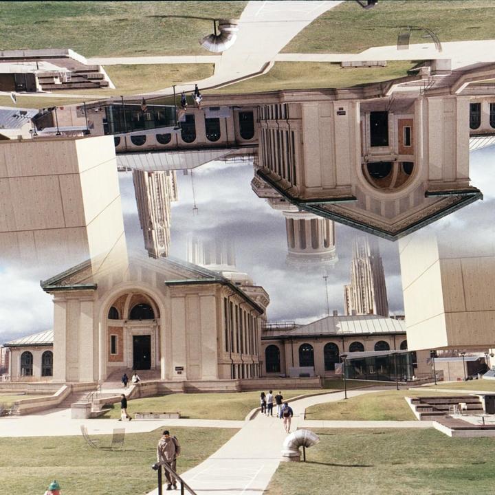 A double exposure shows a building with a green roof and a tall, thin building against a cloudy sky, with people walking on a path in the foreground.