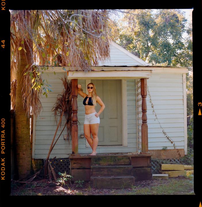A woman stands on a porch next to a palm tree.