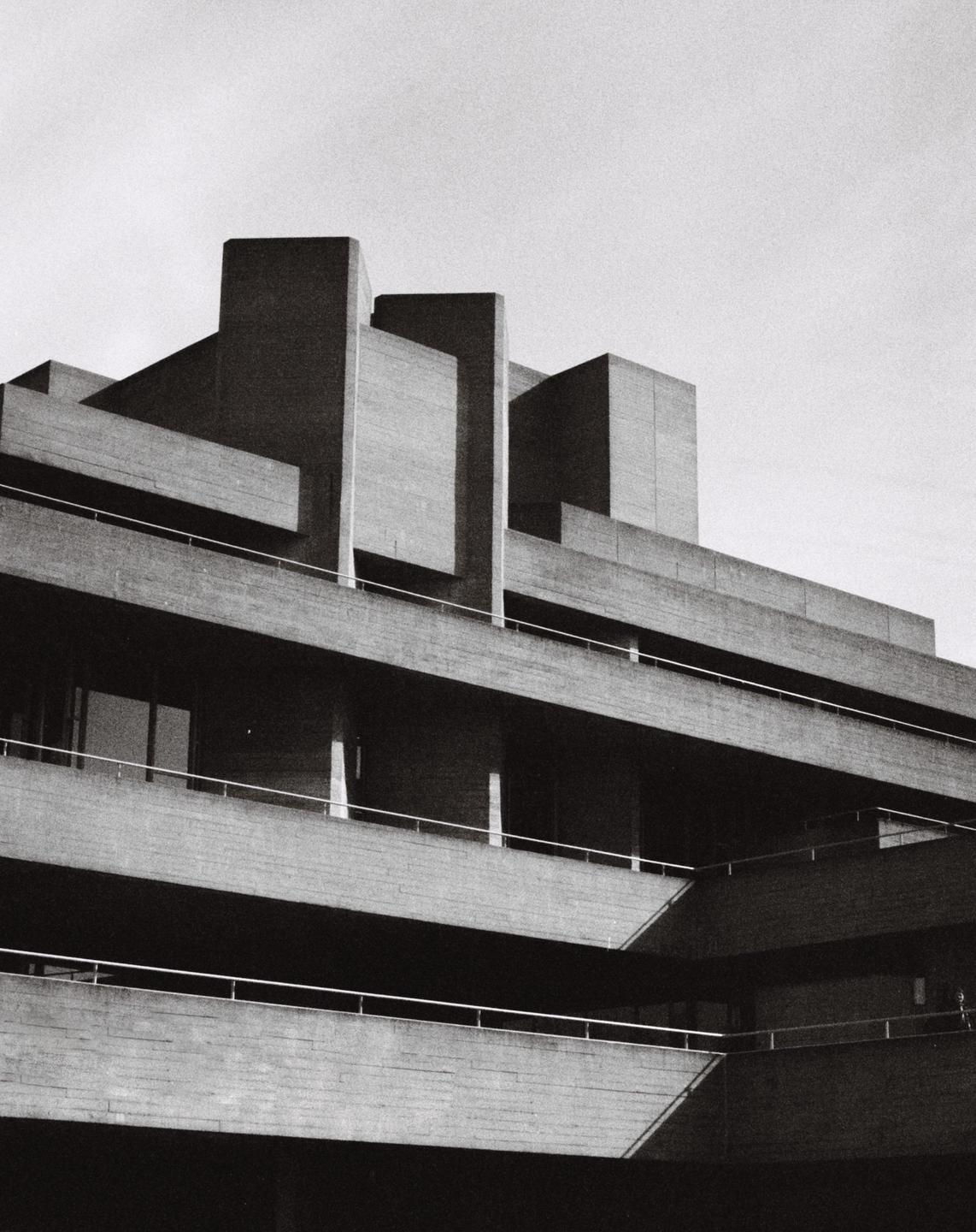 A brutalist building with multiple levels and railings is shown from a low angle.