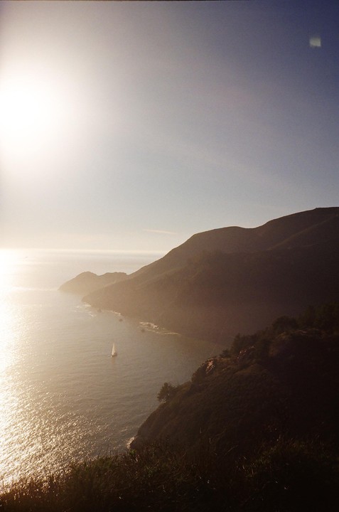 A sailboat is visible on the water below a sunlit mountain range.