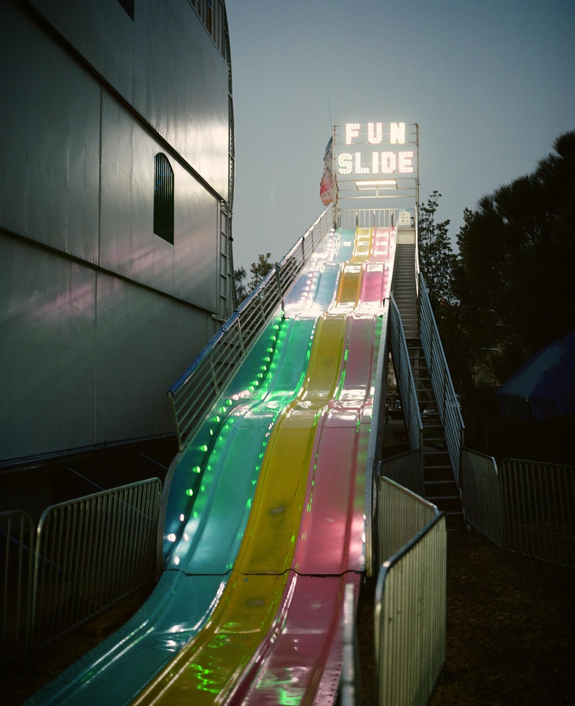 A colorful fun slide with a "FUN SLIDE" sign is illuminated at dusk.