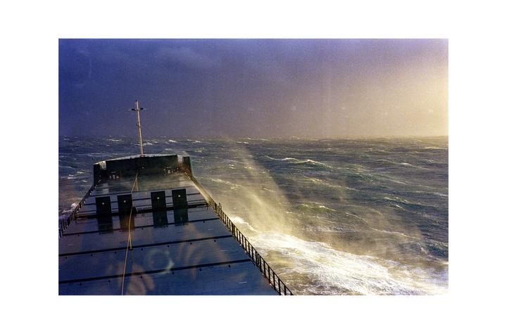 A ship sails through rough seas with spray rising from the waves.