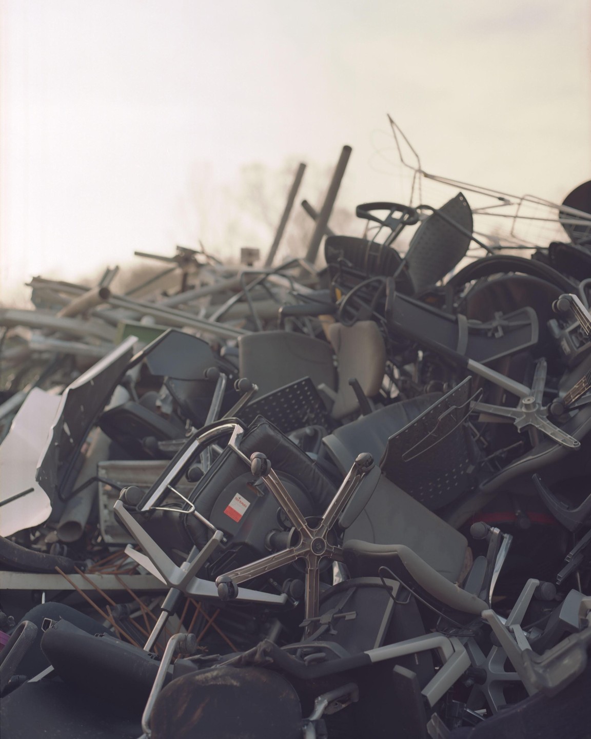 A large pile of discarded office chairs and metal scraps is shown under a bright sky.