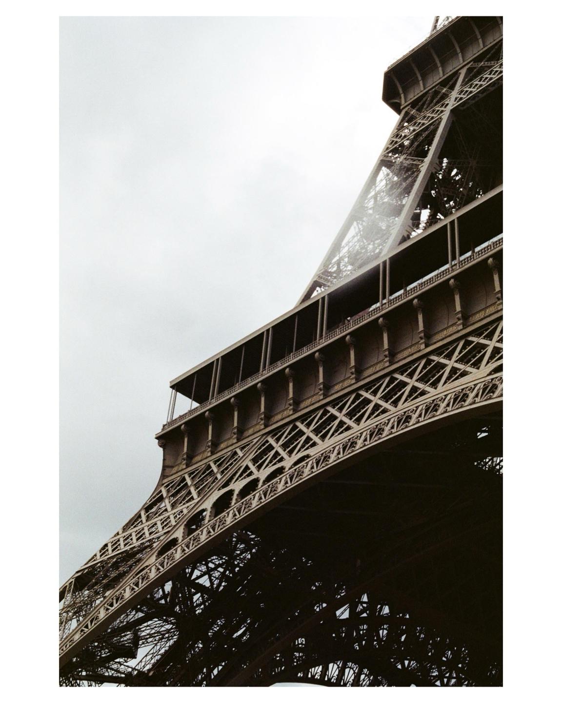 The Eiffel Tower is photographed from below, showing its intricate ironwork against a cloudy sky.