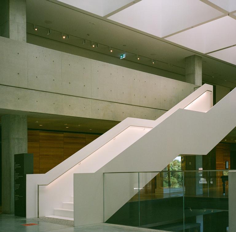 A modern white staircase with illuminated handrails ascends between concrete walls and a glass railing.