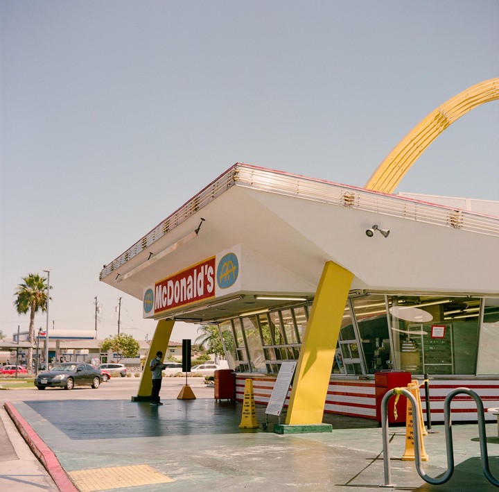 A man stands outside a McDonald's restaurant with a large yellow arch.