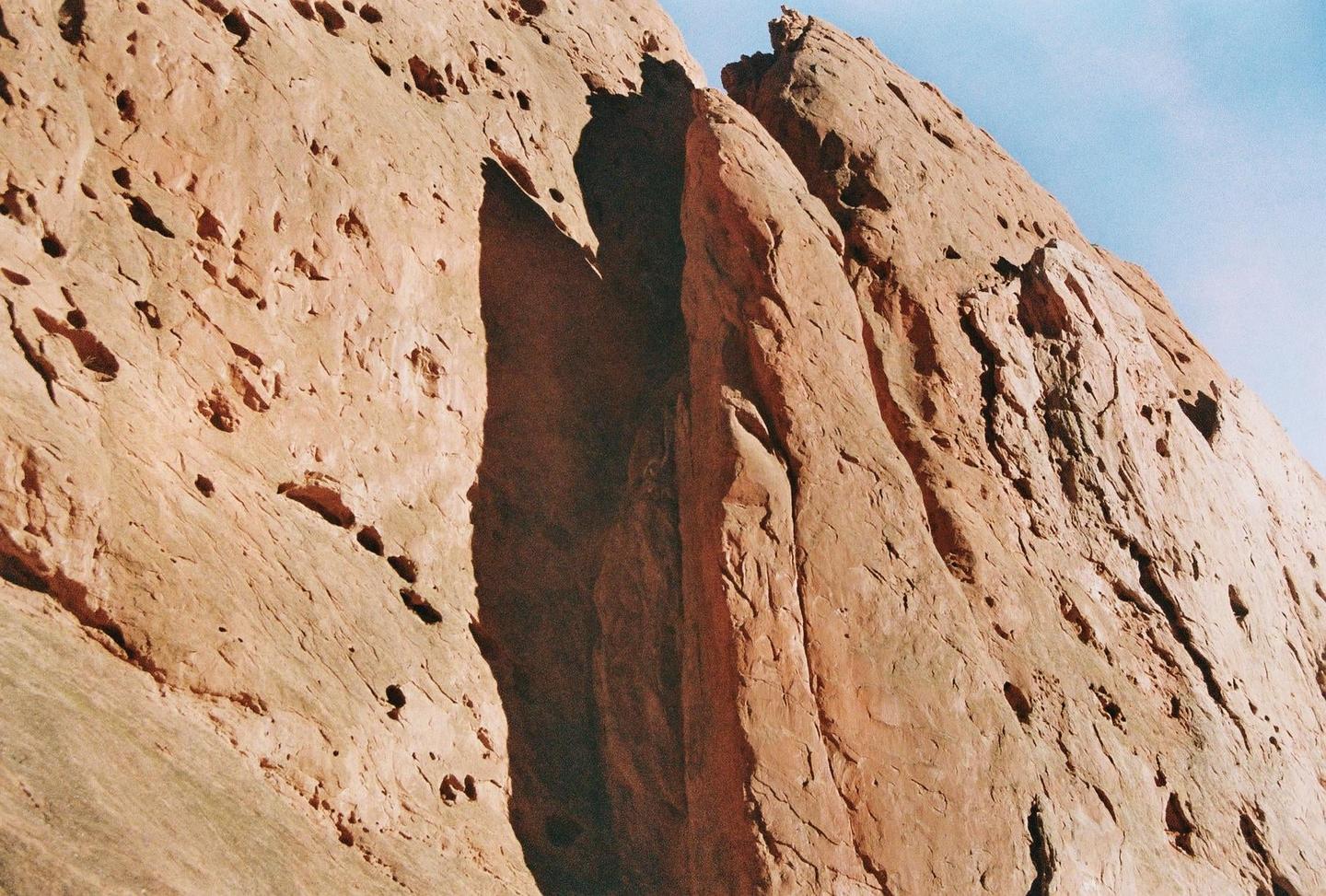 A close-up view of a red rock formation with deep shadows and a bright blue sky.