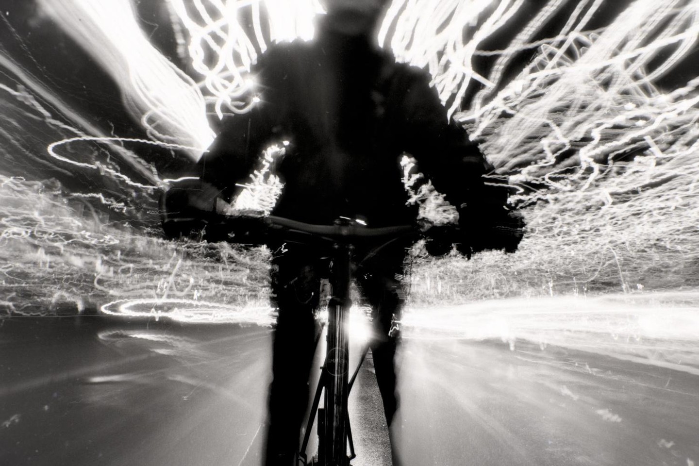A person rides a bicycle at night, creating light trails from movement.